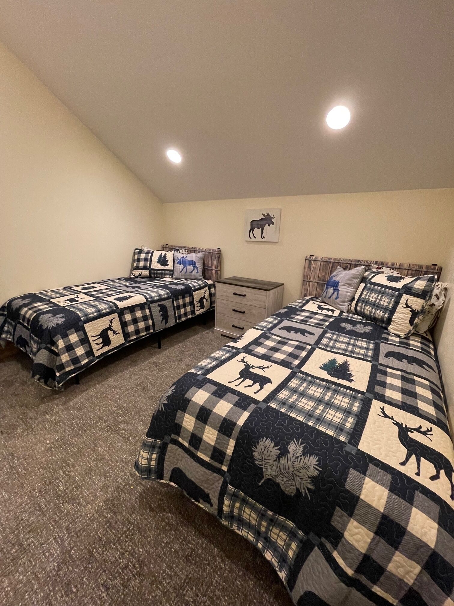 Un dormitorio con dos camas, cada una cubierta con una manta estampada de motivos animales. Se observa un tocador pequeño y un estante montado en la pared.