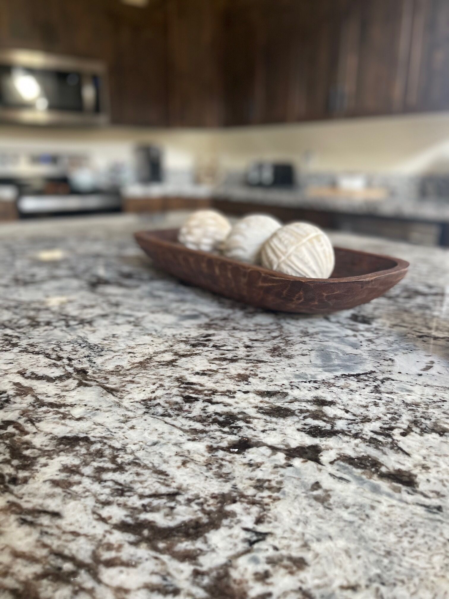 A granite countertop with a wooden bowl containing three white spherical objects.