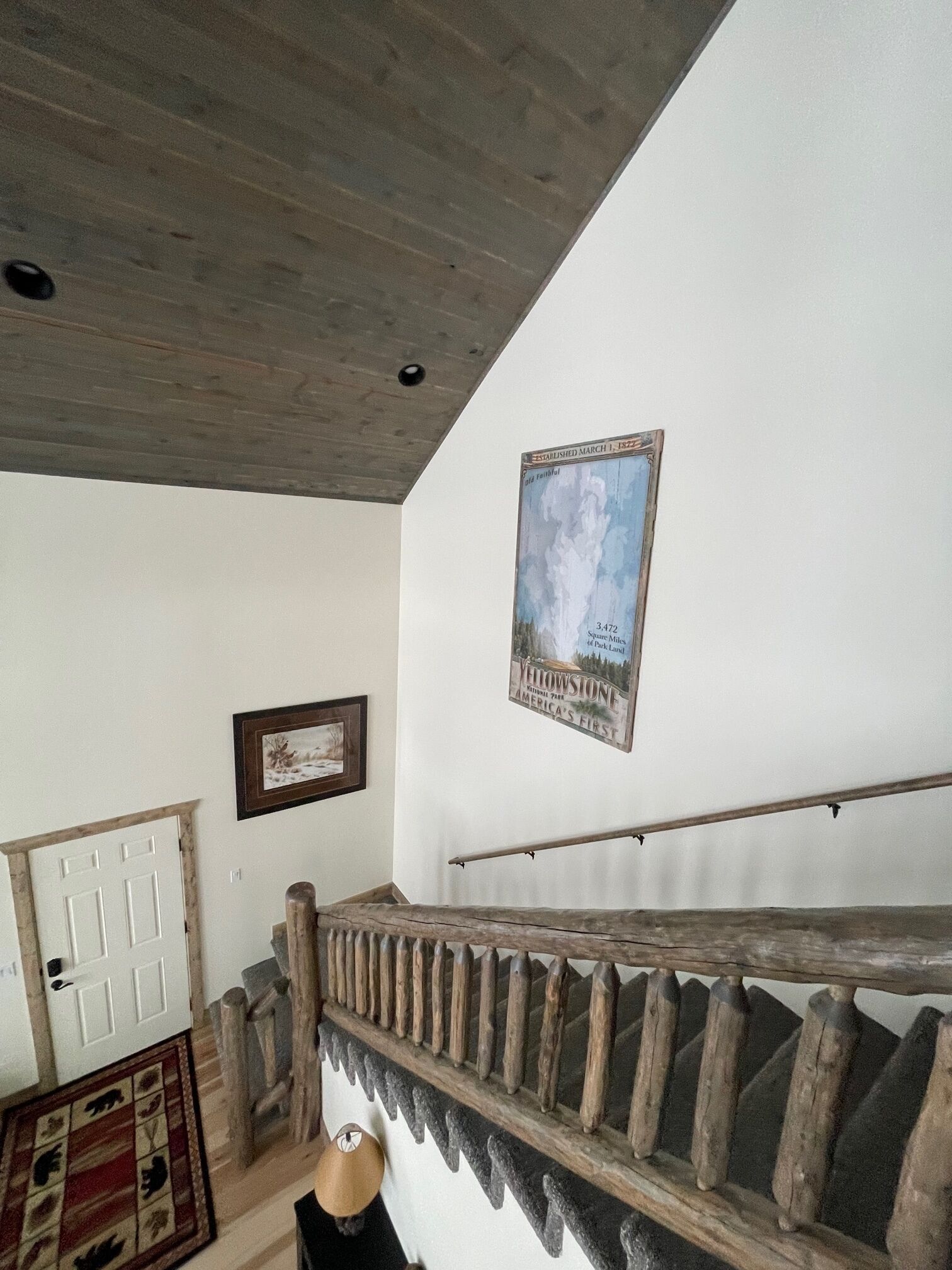 Un escalier avec une rampe en bois et un design rustique, une porte blanche et une plaque fixée au mur indiquant un point de repère dans le parc.