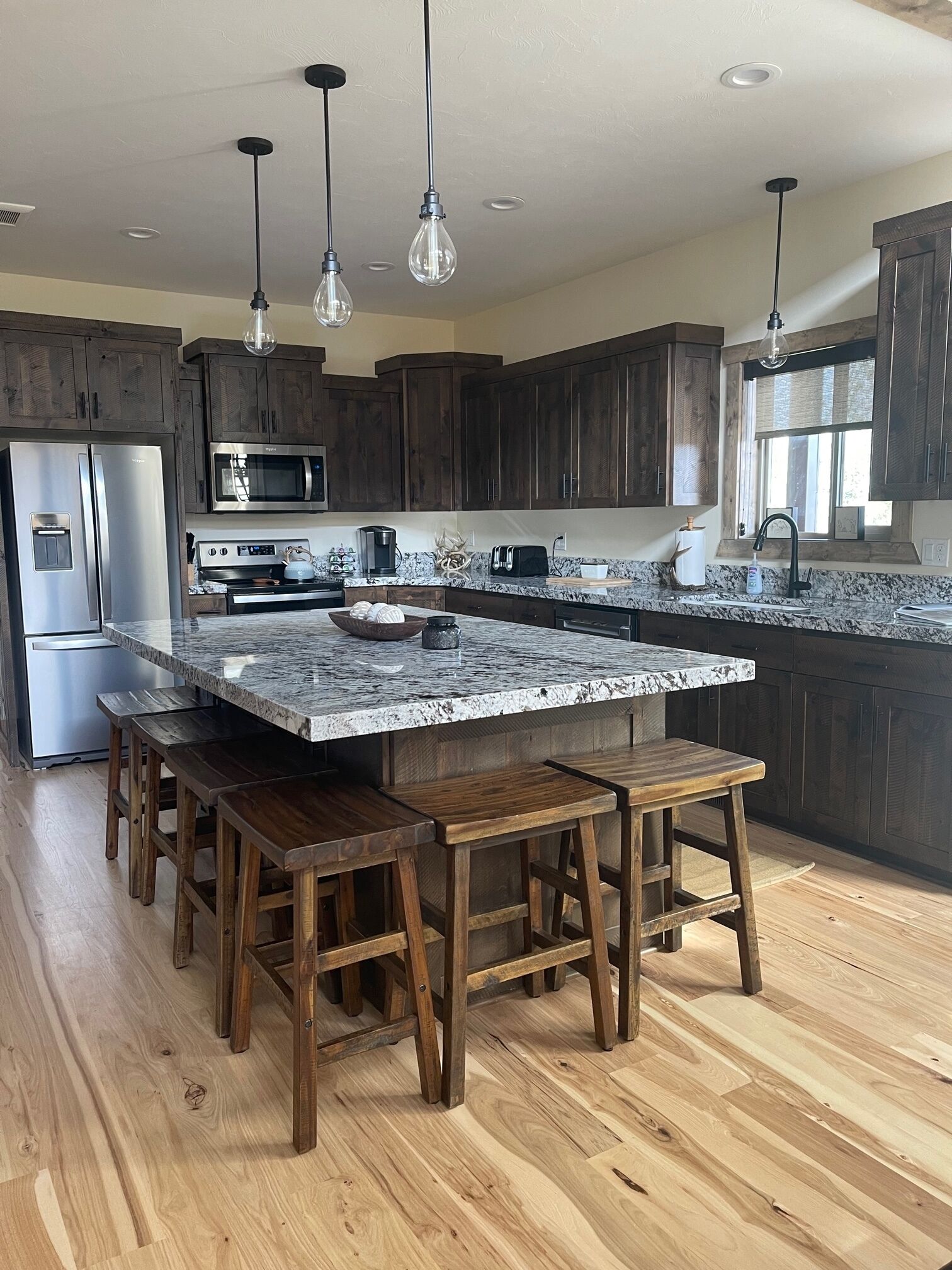 A modern kitchen with dark wooden cabinets, a granite countertop, and a central island with stools.
