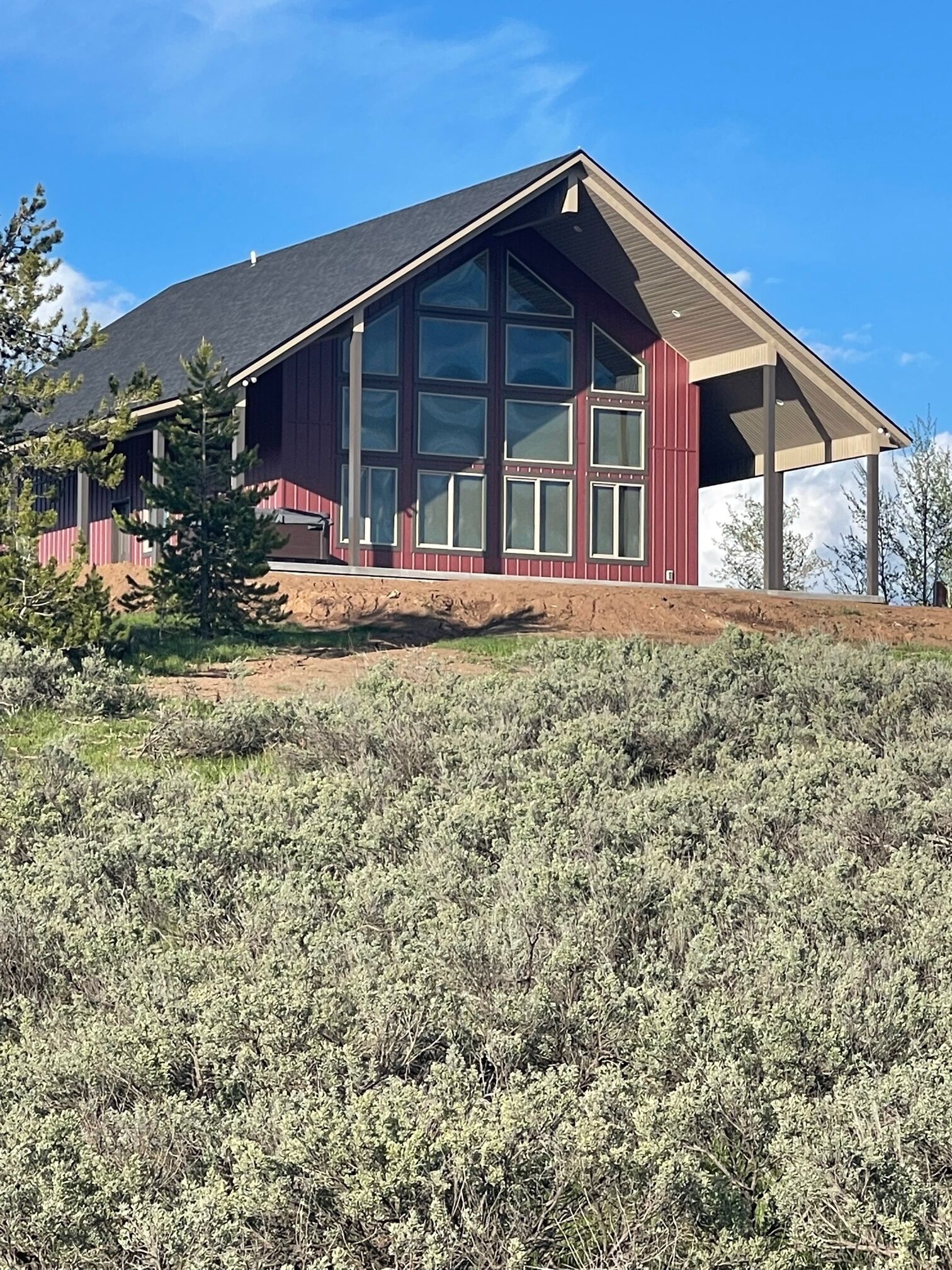 Ein modernes Haus mit großen Fenstern und einem geneigten Dach, umgeben von einer trockenen, buschigen Landschaft.