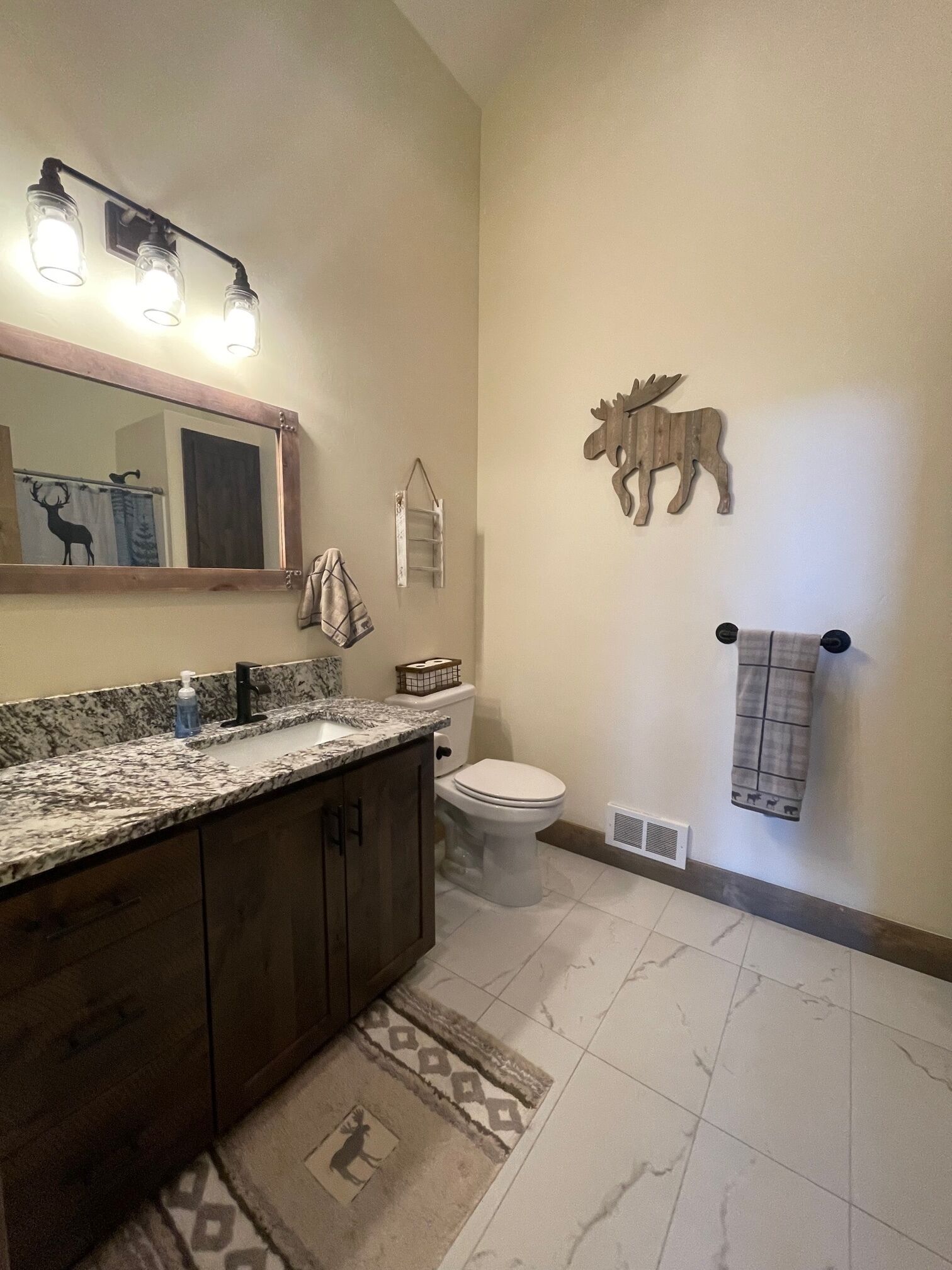 Ein Badezimmer mit Marmorplatte, einem Holzkosmetikschrank, einer Toilette, einem Spiegel und einem Wandhandtuchhalter.