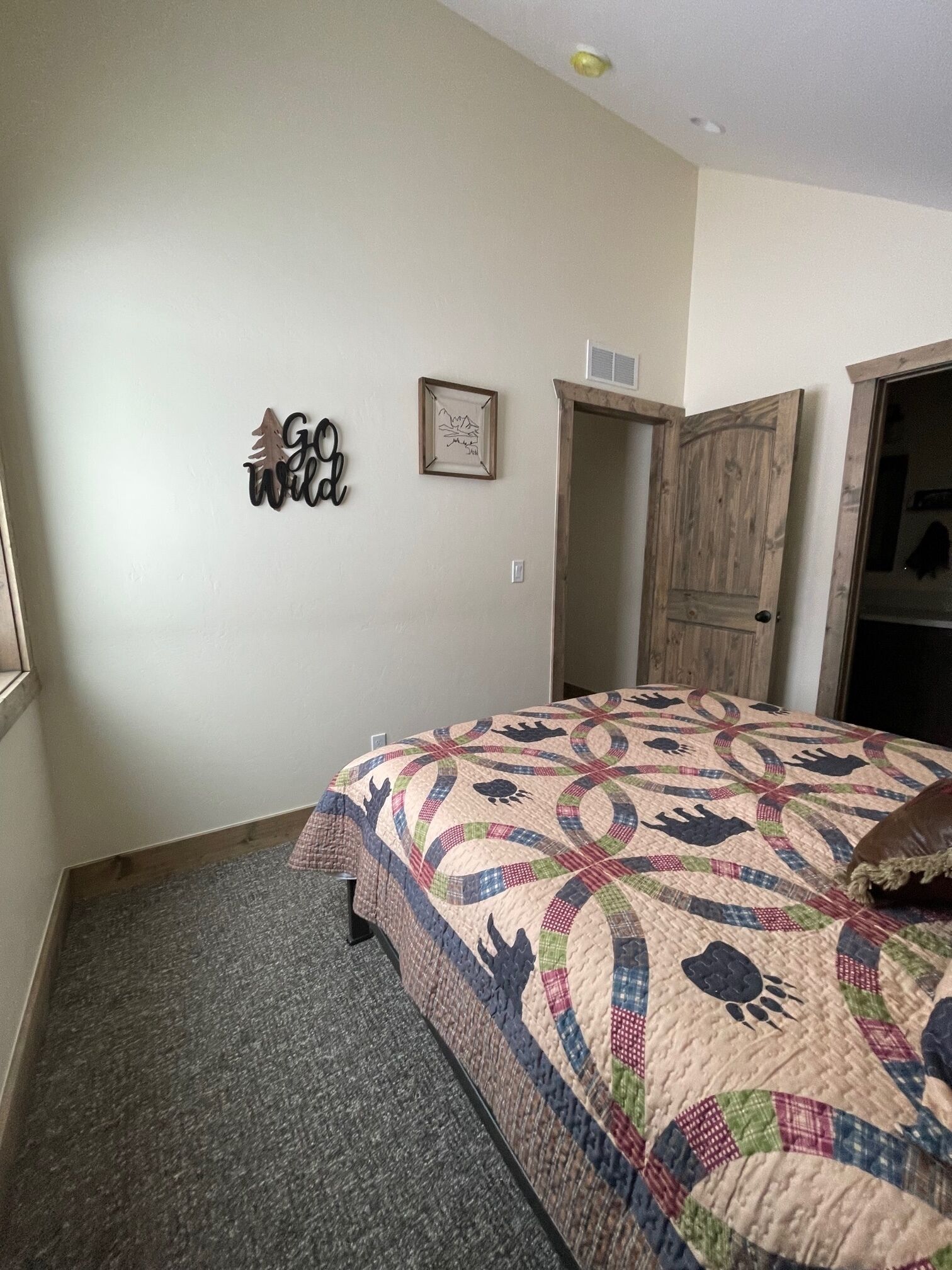 A bedroom with a bed, a wooden door, a wall-mounted sign, and a framed picture.