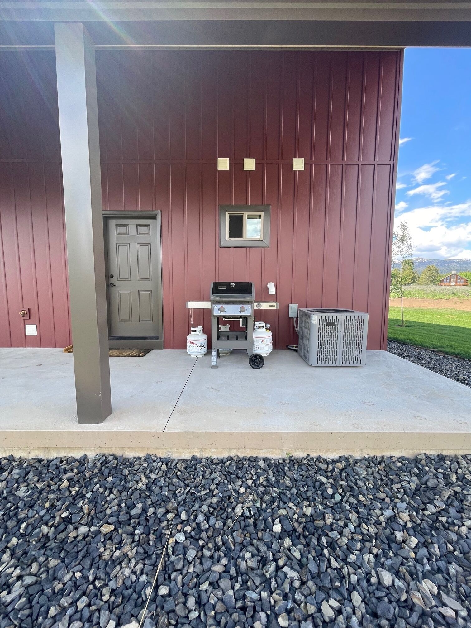 A covered outdoor area with a barbecue grill, propane tanks, and a trash can.