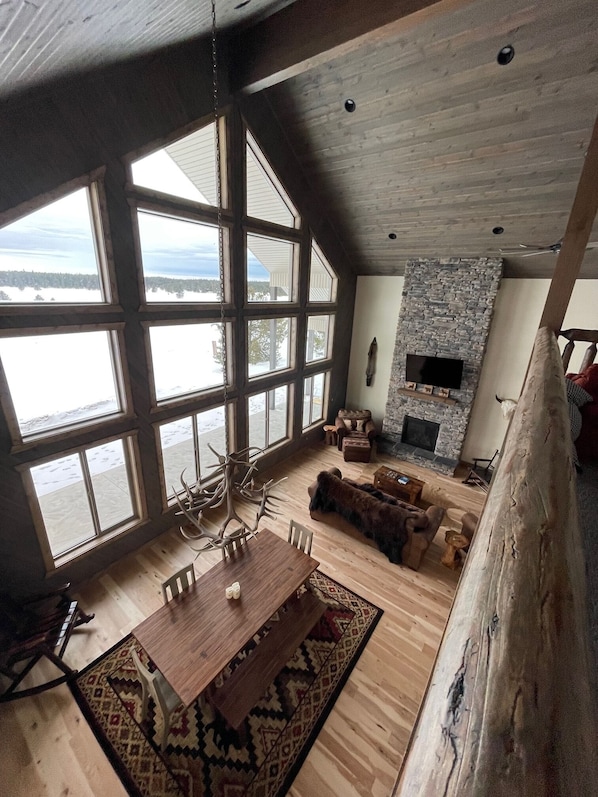 Un salón espacioso con ventanas amplias, una chimenea de piedra y una mesa de comedor de madera.