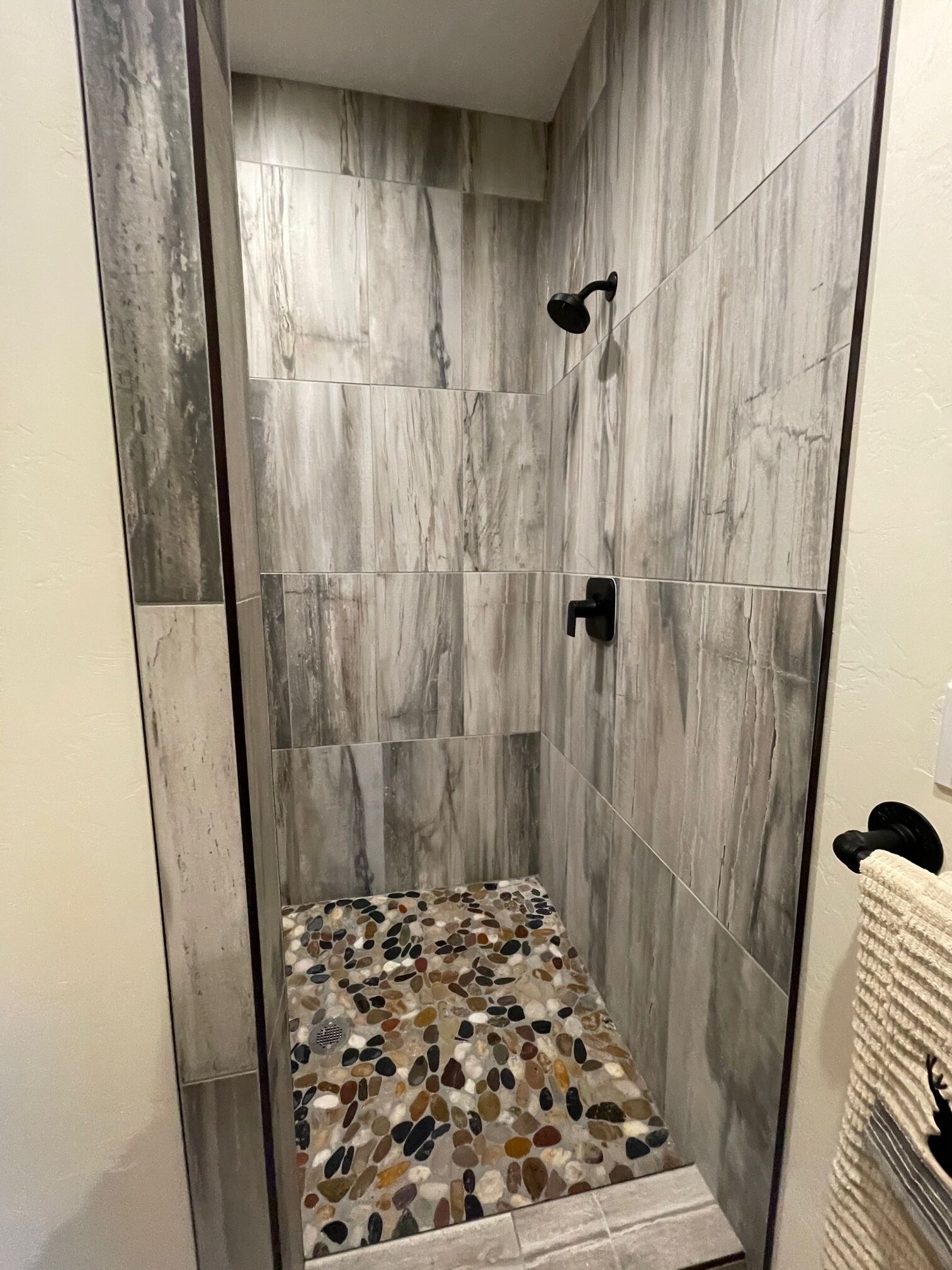 A shower with a pebble-patterned floor and a vertical tile wall.
