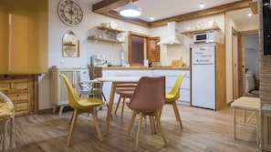 A cozy kitchen with wooden cabinets, a dining table with chairs, a clock, and a refrigerator. - APARTAMENTO RUH SARA (Toledo)