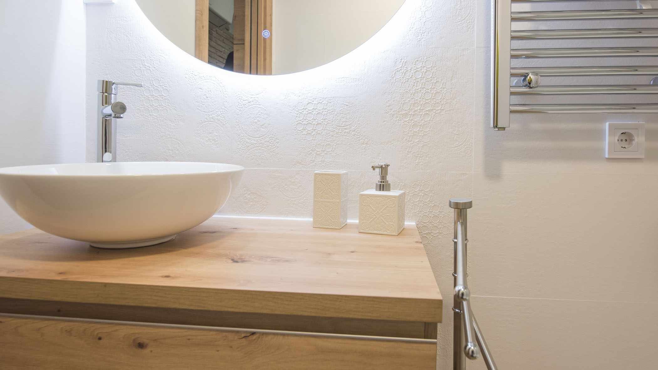 Un baño con un lavamanos blanco de diseño, encimera de madera, espejo y dispensador de toallas.