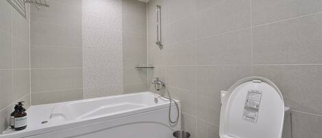 A modern bathroom with a bathtub, toilet, and handrails.