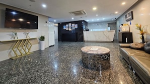 A modern hotel lobby with a reception desk, a flat-screen TV mounted on the wall, a marble coffee table, and a leather sofa. - Platinum Hotel (Busan)