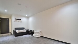 A modern, minimalistic room with a grey sofa, a bed, and a wall-mounted coat rack. - Platinum Hotel (Busan)