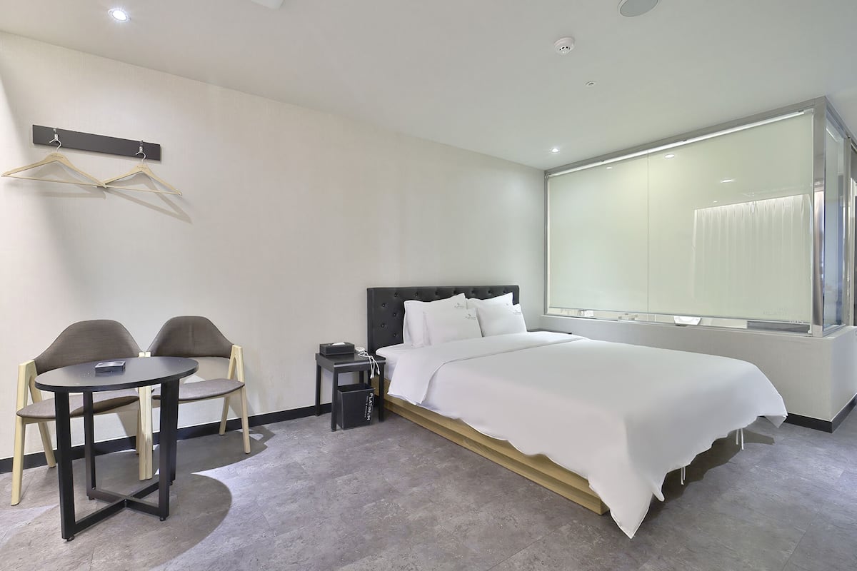 Habitación de hotel moderna con cama, mesita de noche, dos sillas, una pequeña mesa y perchero.