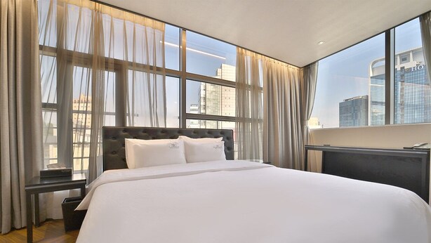 A hotel room with a large bed, a desk, and a view of the city through large windows. - Platinum Hotel (Busan)