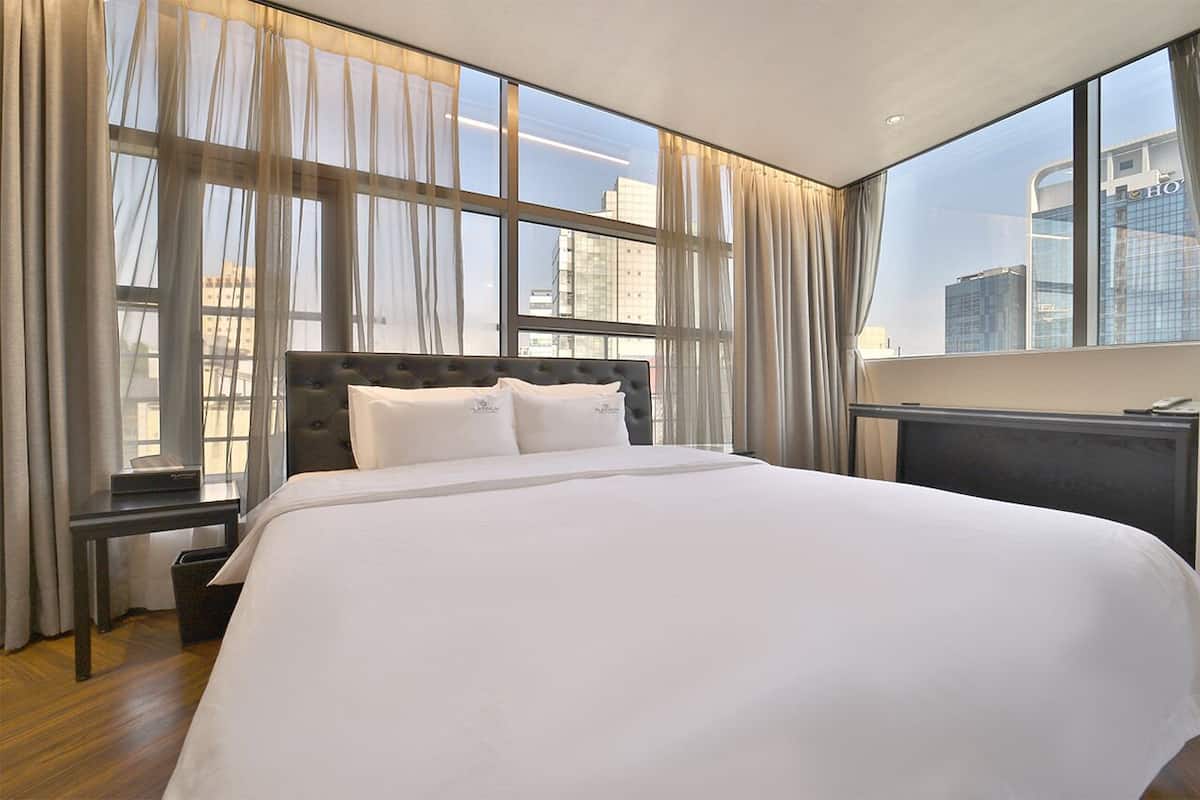 Habitación de hotel con una cama grande, un escritorio y vistas de la ciudad a través de amplias ventanas.
