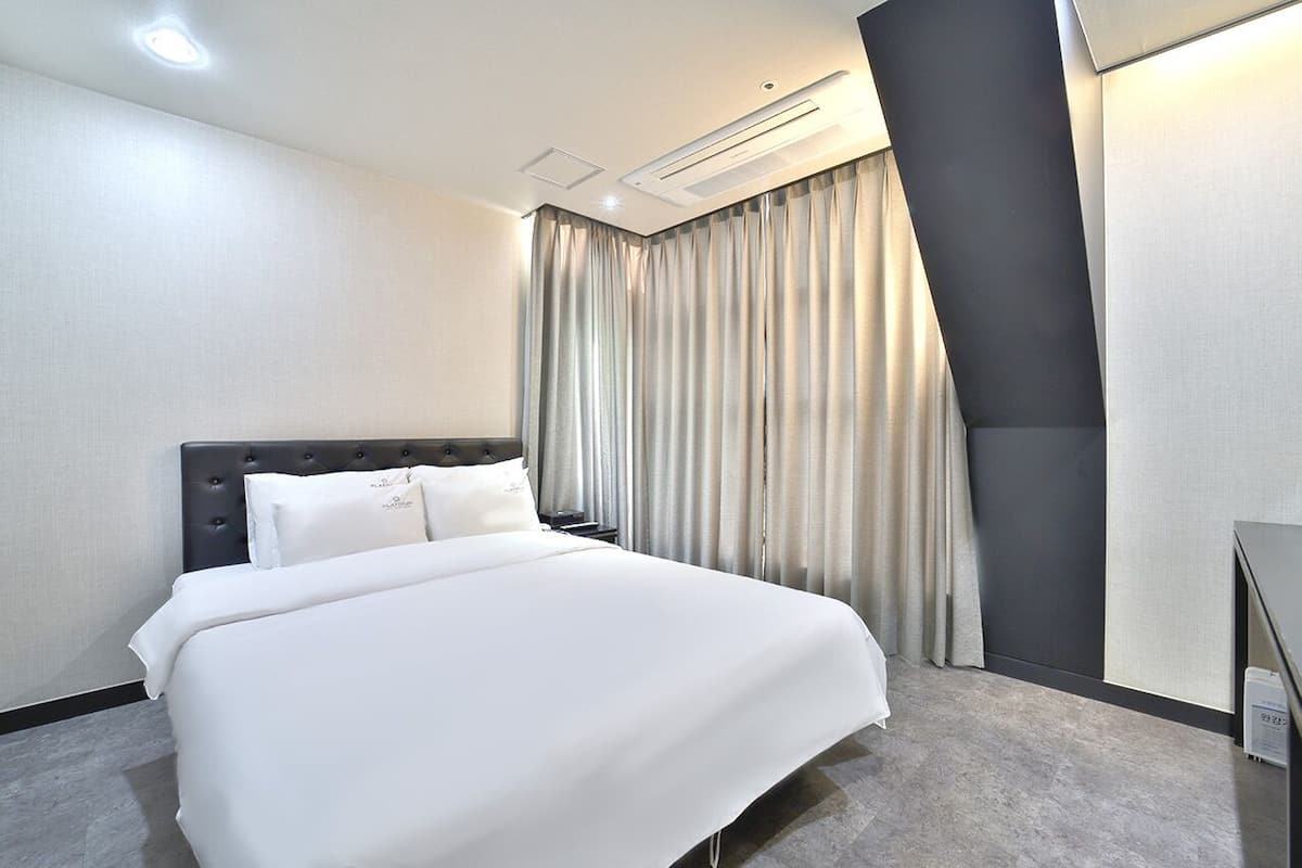 Una habitación de hotel con una cama grande, una mesita de noche, un escritorio y una cortina.