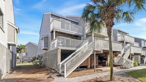 A modern multi-story residential building with a central staircase, balconies, and a small outdoor area with a palm tree. - CapeSanBlas Bright, End Unit •Short walk to neighborhood private beach •2 Pools  (Port St. Joe)