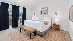 A bedroom with a bed, a bench, a bedside table with a lamp, a ceiling fan, and a balcony with curtains. - CapeSanBlas Bright, End Unit •Short walk to neighborhood private beach •2 Pools  (Port St. Joe)