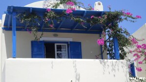 A building with a white facade, blue shutters, and pink flowers. - Santorious Nice View Apartment (Santorini)