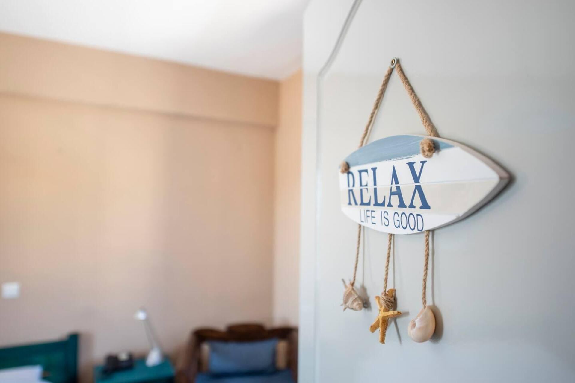 A wall with a decorative sign that reads "RELAX RELAX LIFE IS GOOD" and two seashells hanging below it.