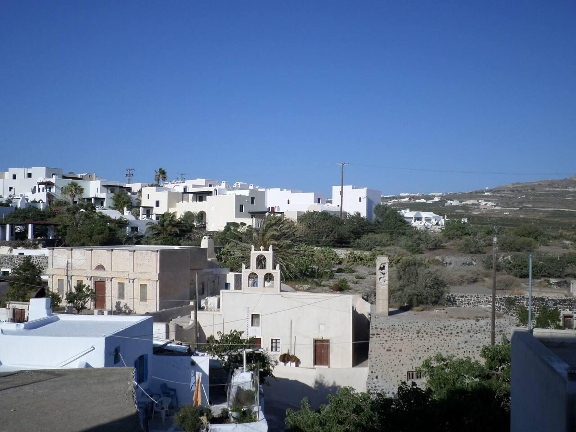 A coastal town with white buildings, a church with a bell tower, and a clear blue sky.
