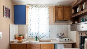 A compact kitchen with wooden cabinets, a white countertop, a small sink, and a coffee maker. - Santorious Nice View Apartment (Santorini)