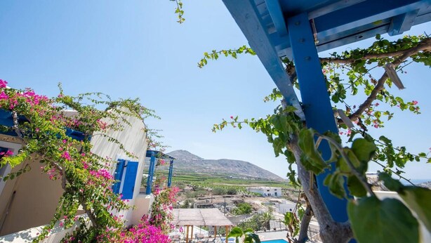 A coastal view with a clear sky, a mountain in the background, and a building with blue shutters and pink flowers. - Santorious Nice View Apartment (Santorini)