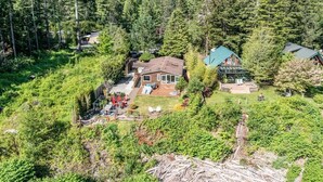 Ein großes Haus, umgeben von dichtem Wald, mit einer Terrasse und einer Sitzgelegenheit im Freien.
