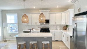A modern kitchen with white cabinets, a stainless steel refrigerator, a large island with stools, and pendant lighting. - Beautiful townhome in Wildwood Crest, walking distance to beach (Wildwood)