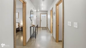 Un pasillo con puerta de madera, un espejo y una pequeña mesa con un florero.