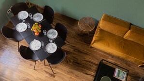 Un coin repas avec une table dressée pour quatre personnes, entourée de chaises noires. Une petite table ronde avec une chaise en osier se trouve à côté d’un canapé.