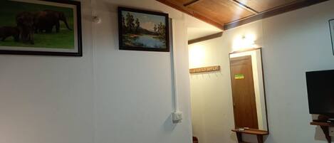 A room with a wooden ceiling, a framed painting of elephants, a framed landscape painting, a mirror, and a television.