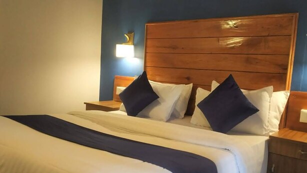 A neatly made bed with a wooden headboard, white bedding, and dark blue pillows. - Winter gardens mountain room (Munnar)
