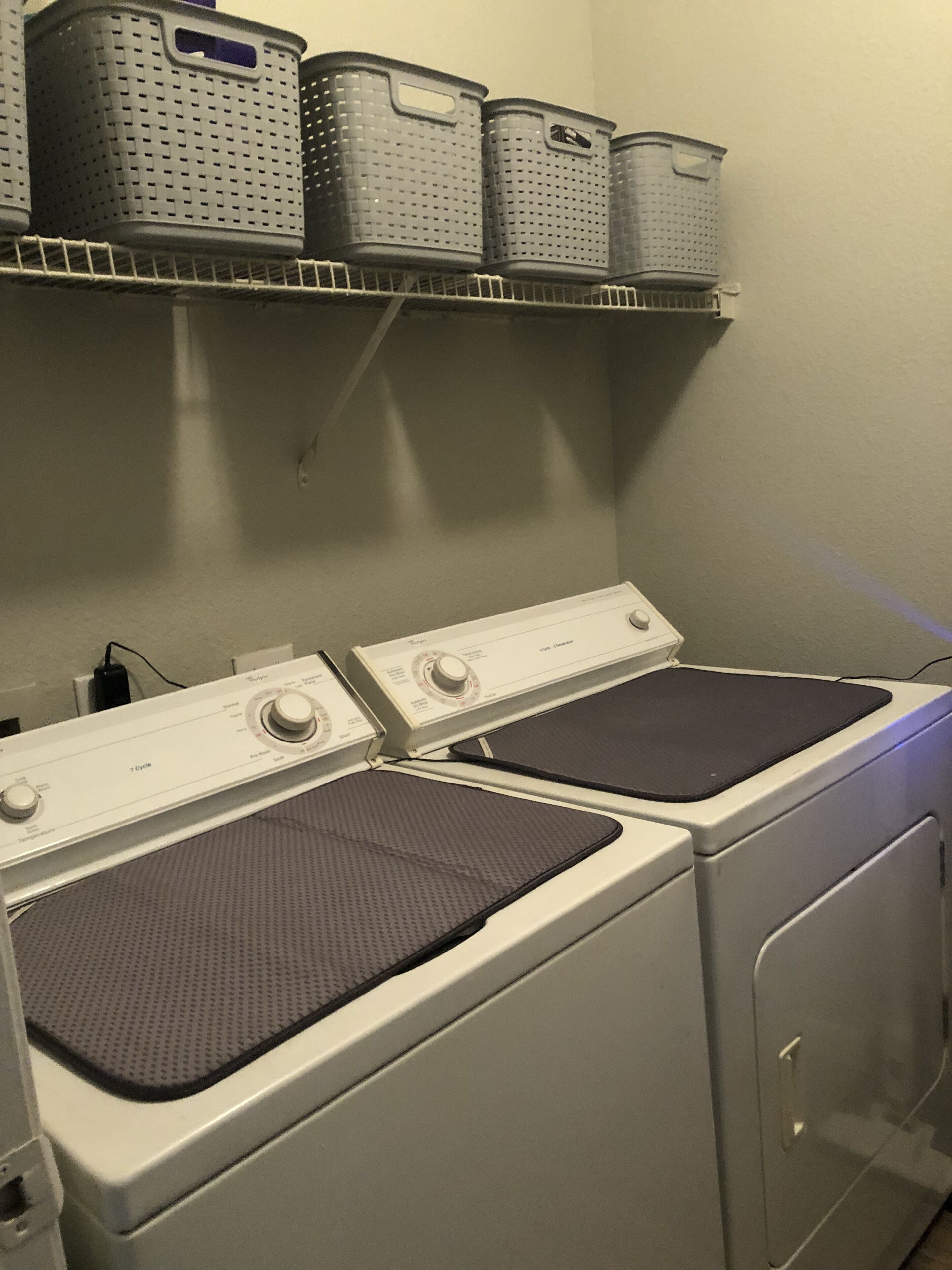 A laundry area with two washing machines and a shelf above containing laundry baskets.