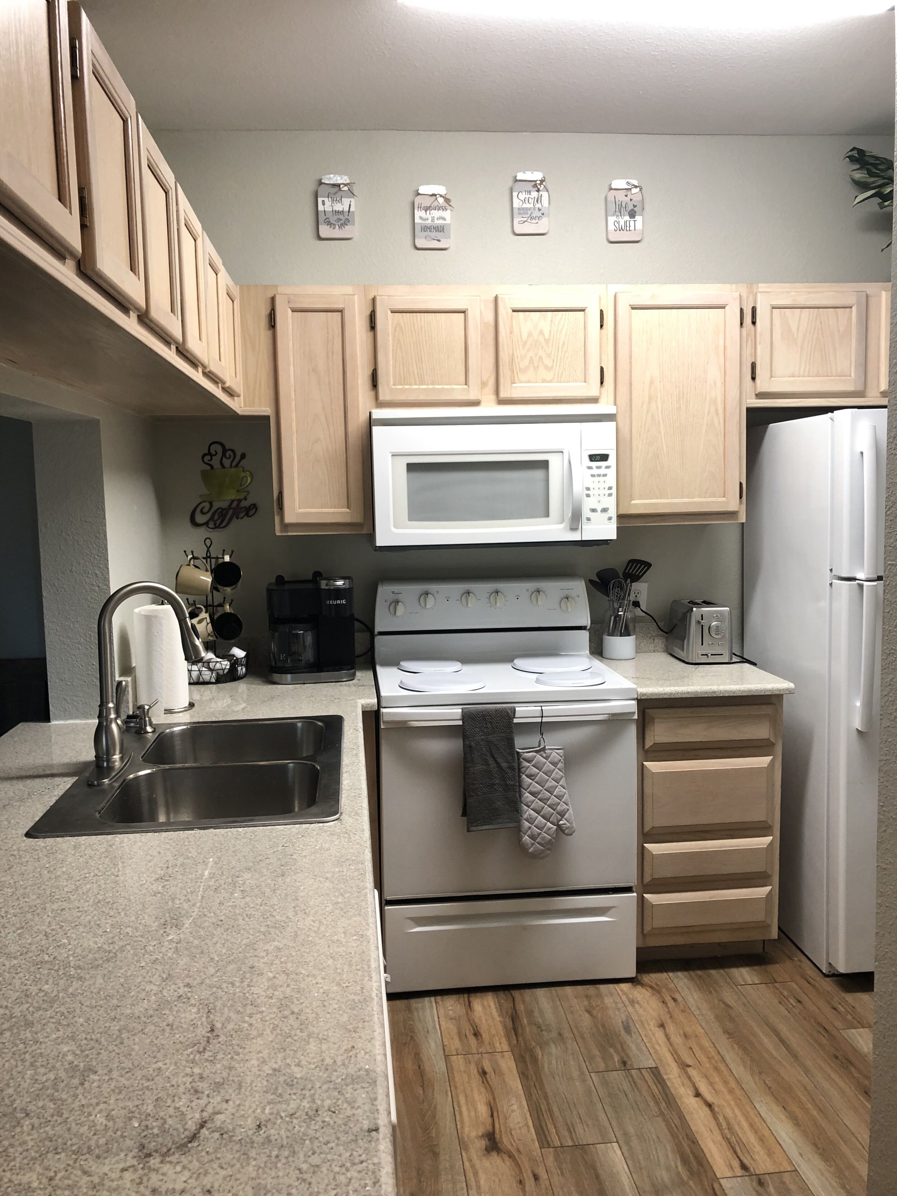 A compact kitchen with wooden cabinets, a white microwave, a stove, a sink, and a refrigerator.