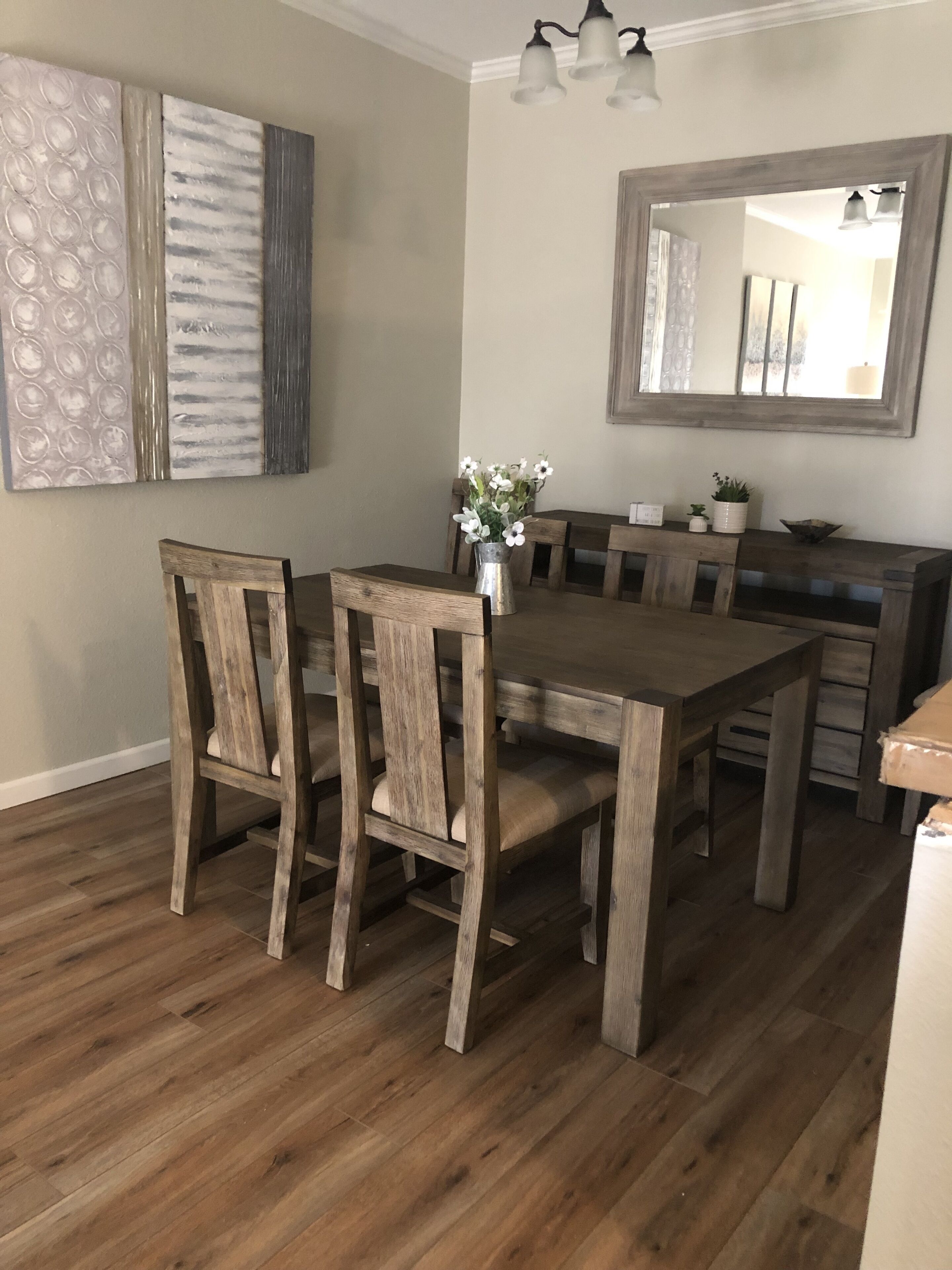 A dining area with a wooden table and chairs, a vase with flowers, and a mirror on the wall.