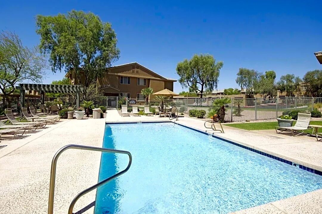 A swimming pool with lounge chairs and umbrellas, surrounded by a fence and trees.