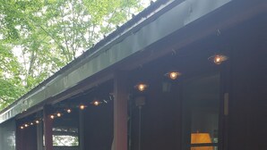 Een overdekt terras met een houten dek, een bank en een stapel haardhout.