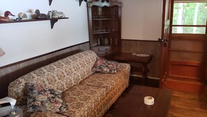 Een woonkamer met een bloemenbank, een houten salontafel, een kast met glazen erin, en een houten deur.