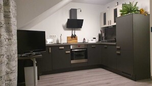 Une cuisine moderne avec des meubles de couleur sombre, un four encastré, un four à micro-ondes et un téléviseur à écran plat fixé au mur.