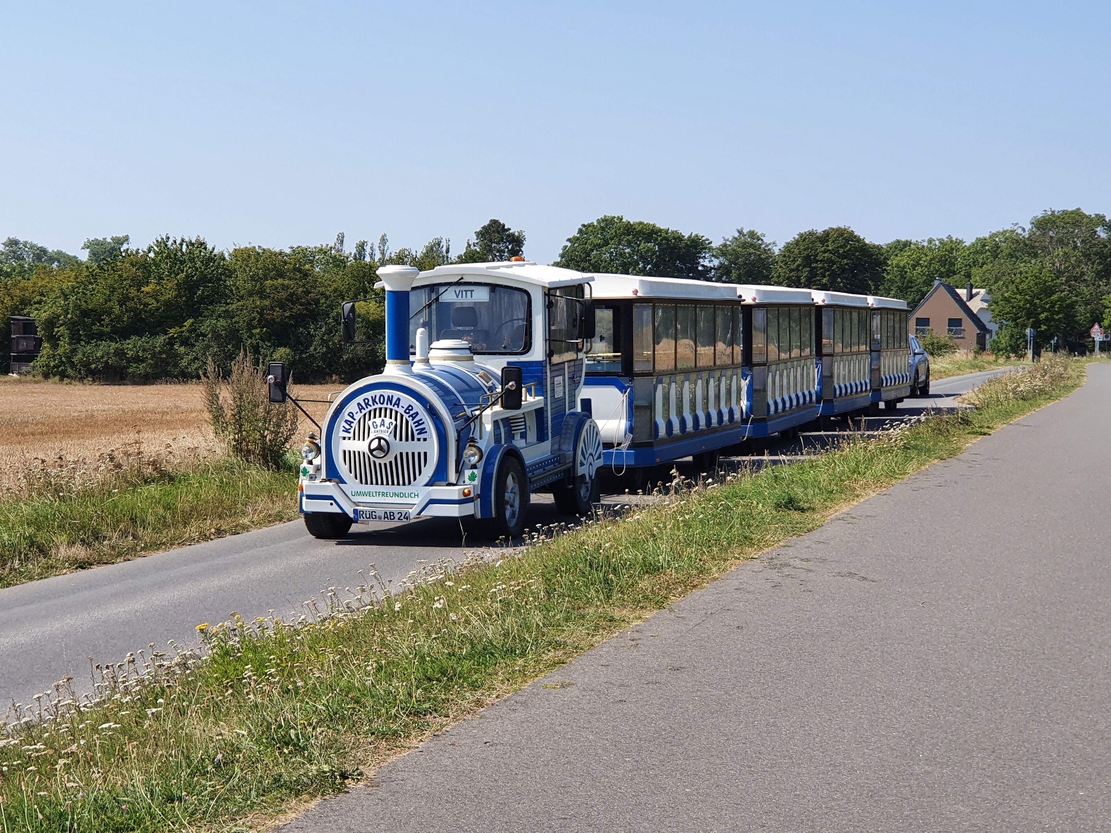 Un tren antiguo azul y blanco con un diseño clásico, viajando por un camino rural.