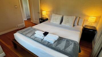 A hotel room with a large bed, two bedside tables with lamps, wooden flooring, and a door leading to another room.
