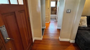 A hallway with wooden flooring, a brown door, and a dark-colored couch.