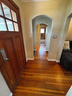 A hallway with wooden flooring, a brown door, and a dark-colored couch. - Cozy, Convenient Holladay Bungalow w/ Amenities (Salt Lake City)