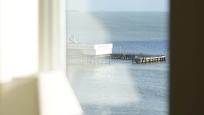 Une vue depuis une fenêtre donnant sur une jetée qui s’avance dans des eaux calmes.