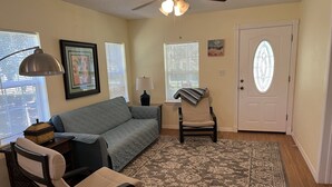A living room with a sofa, a chair, a rug, a lamp, and a door with a stained glass window.