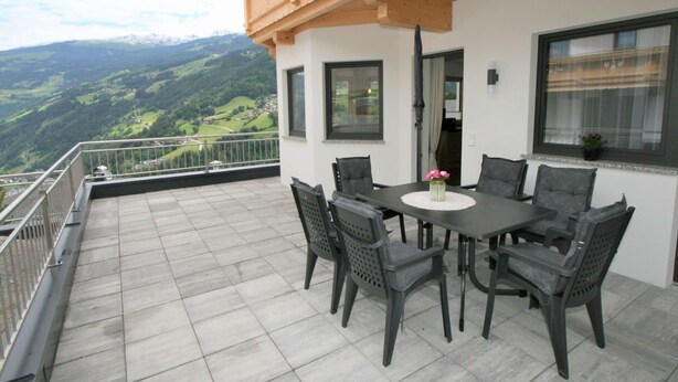 Ein Balkon mit Tisch und Stühlen, mit Blick auf eine gebirgige Landschaft.