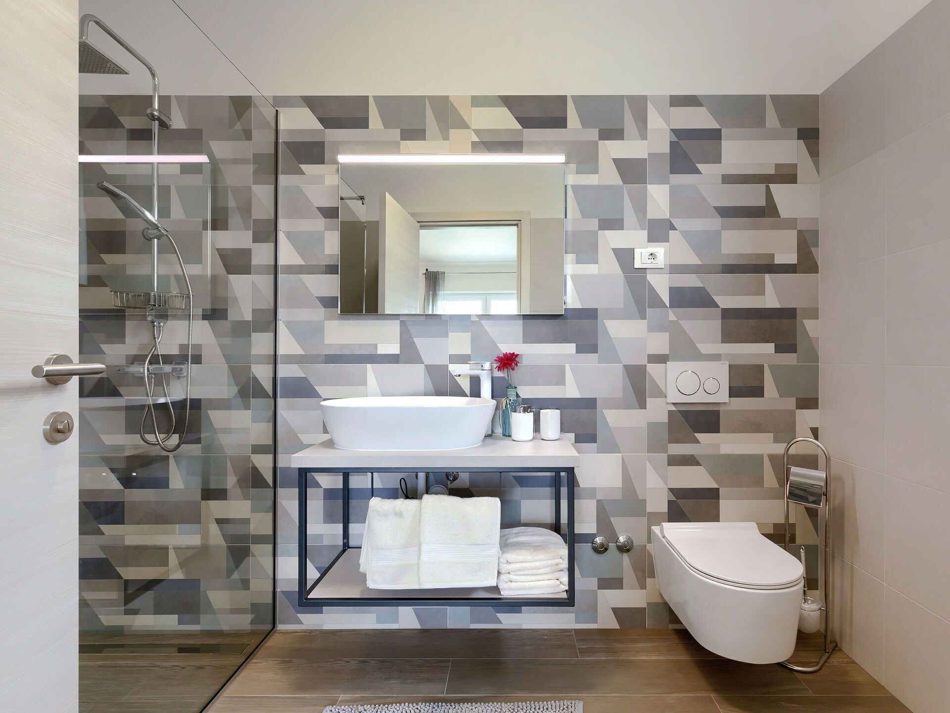 Een moderne badkamer met een douchecabine van glas, een witte wastafel en een toilet.