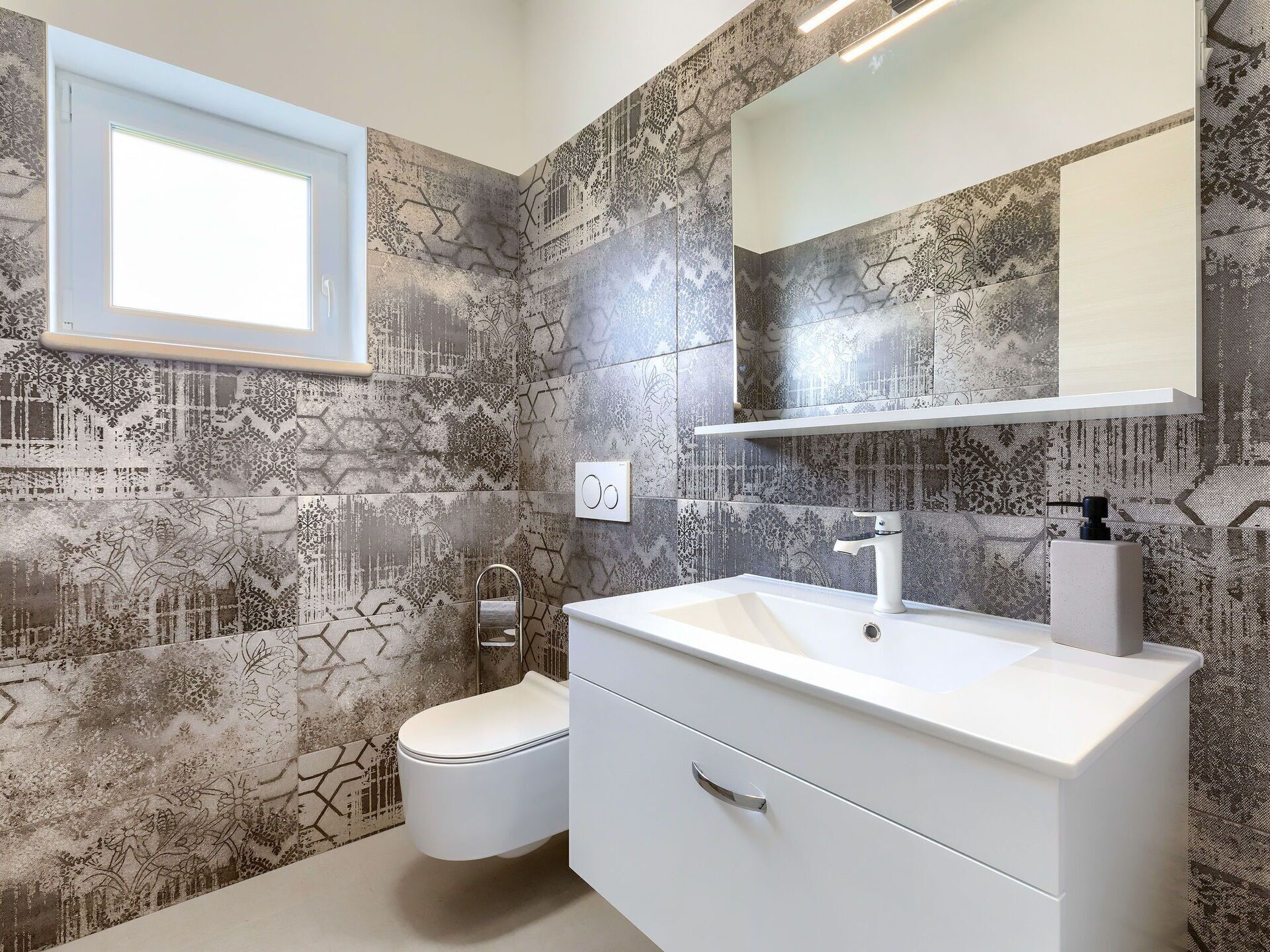 A bathroom with patterned tiles, a white sink, a mirror, and a toilet.