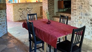 Une salle à manger au sol en pierre, avec une nappe rouge, des chaises en bois et un vase rempli de fleurs.