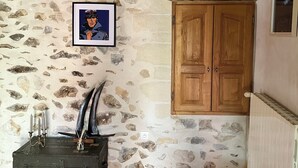 Une pièce aux murs de pierre, avec une armoire en bois, un tableau encadré et une boîte métallique verte.
